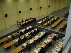 A session of the municipal council in which decisions to implement the city’s new statute are taken. Here, the consociational power-sharing script is played out and played upon by elected councilors representing ethno-nationally defined interests while being observed and counseled by members of the Mostar Implementation Unit